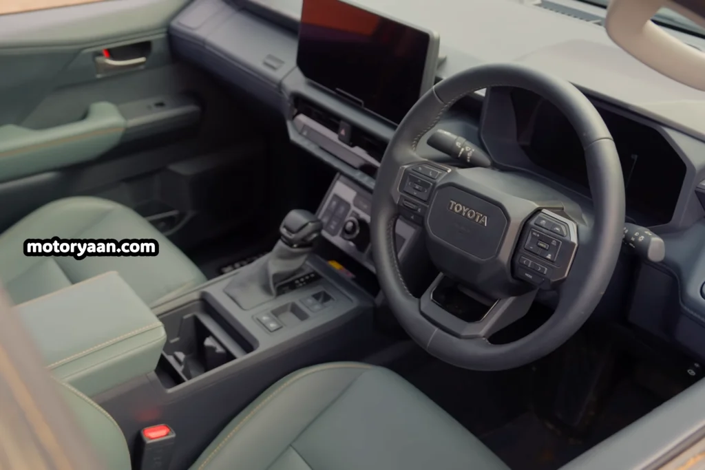 2026 Toyota Hilux dashboard interior showing steering wheel, digital instrument cluster, infotainment, center console, and front seats.